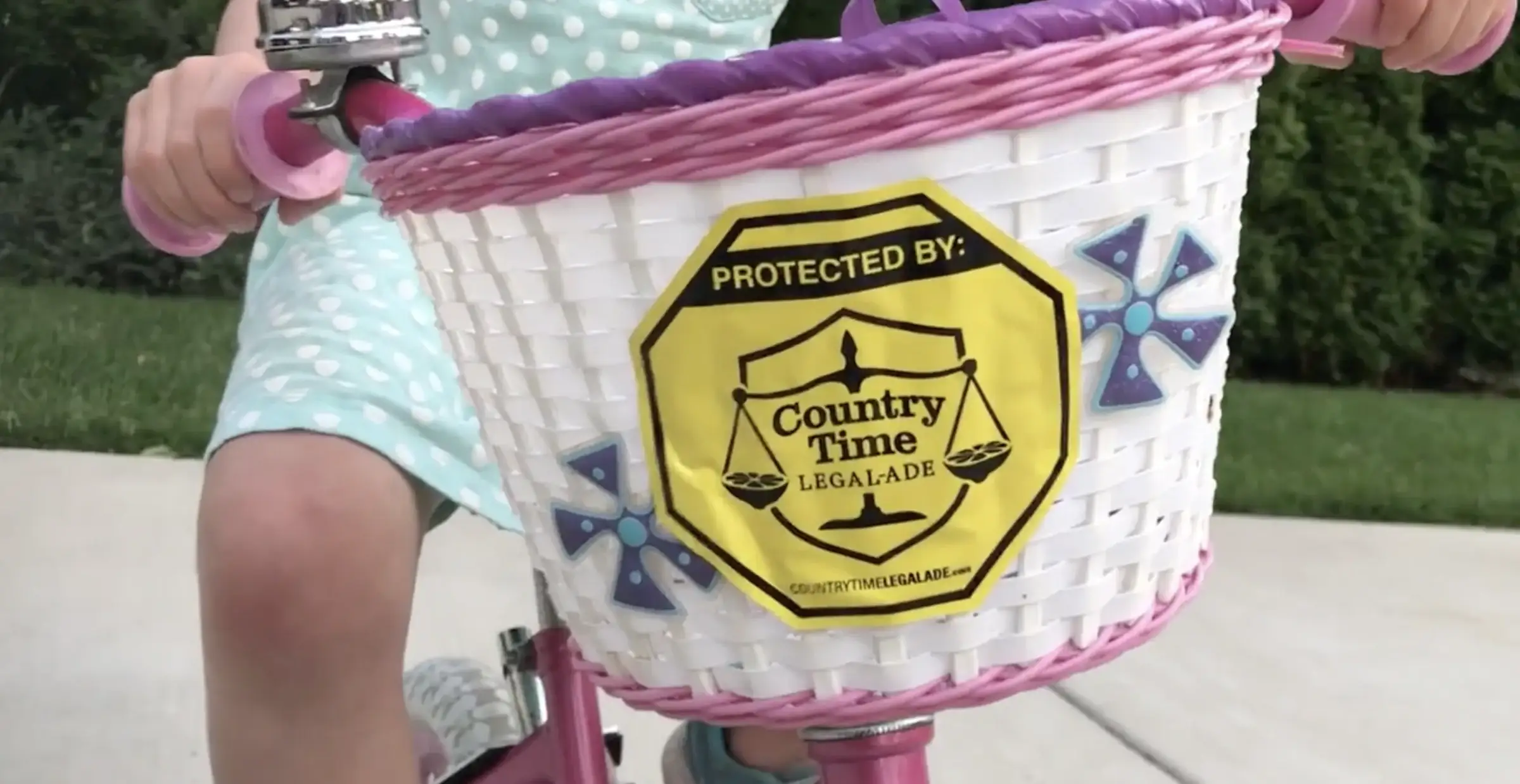 'Protected by Country Time Legal-Ade' badge on a bike basket (case film still)