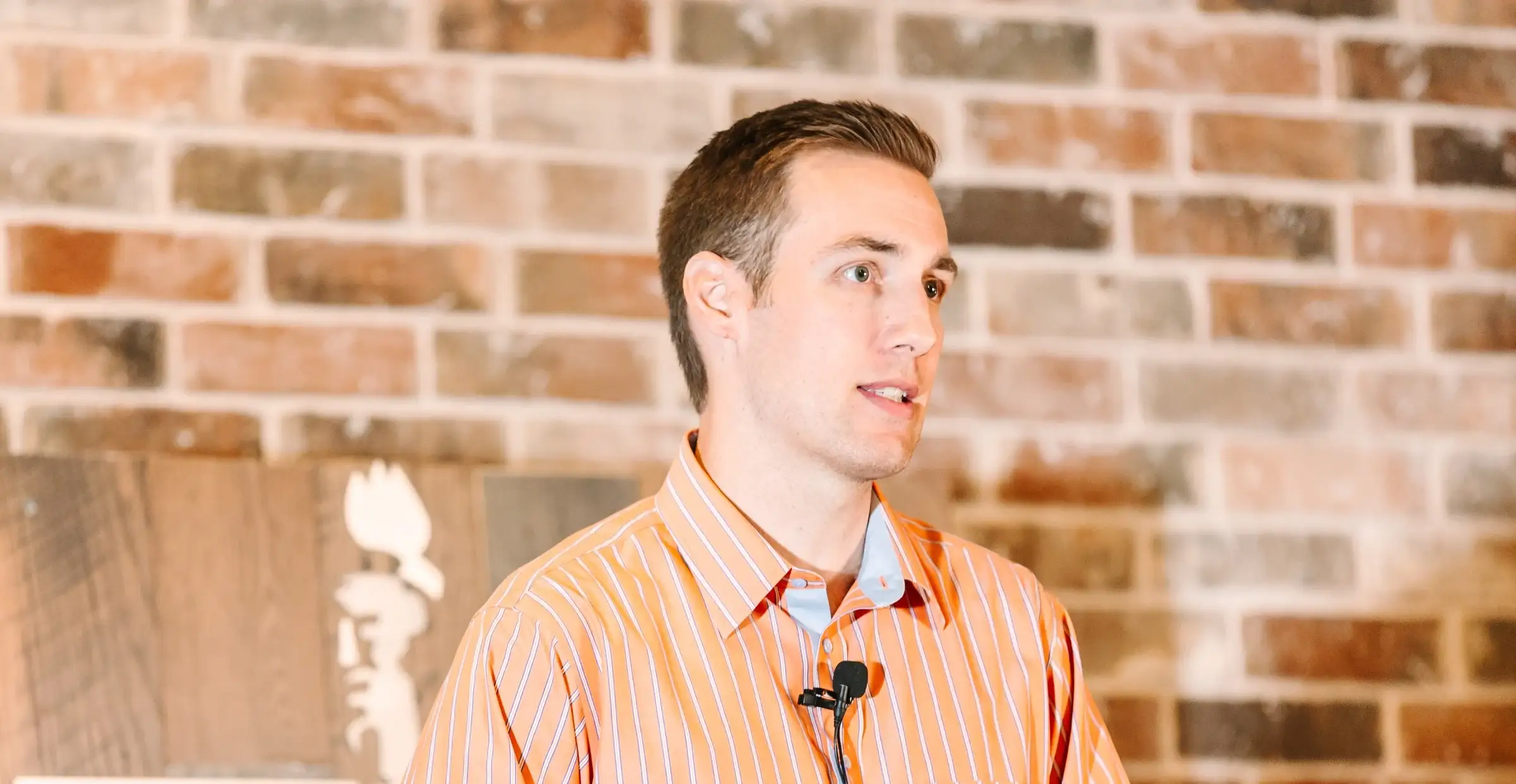 Jared Young in an orange shirt in front of a brick wall painted with the Statue of Liberty
