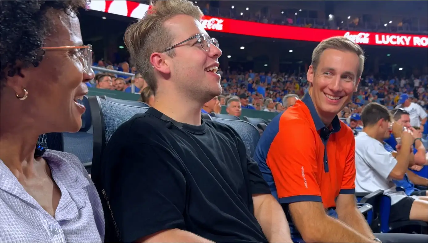 Kirby and Luke laugh with Jared Young, in an orange polo, in the stands at the Royals game