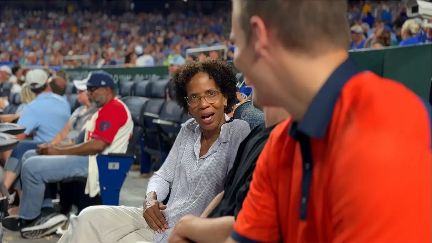 Kirby smiles at Jared Young, in an orange polo, as they talk during the Royals game